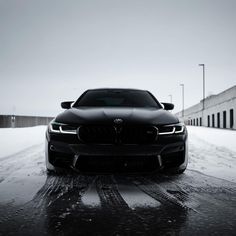 the front end of a black bmw car on a snowy road