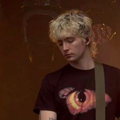 a young man with blonde hair wearing a black t - shirt and holding a guitar