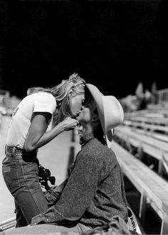 black and white photograph of two women sitting on bleachers at night, one with her hat over her head