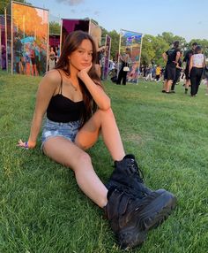 a woman sitting on the grass with her legs crossed and looking at the camera,