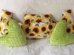 three pillows and two green pears on a white bed with sunflowers in the background