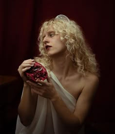 a woman wearing a tiara is holding a red object in her hands and looking off to the side