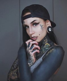 a woman with tattoos and piercings on her face is posing for the camera while wearing a baseball cap