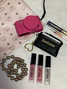 the contents of a purse are laid out on a bed, including lip glosses and a camera