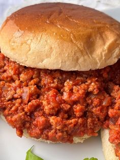 a sloppy joe sandwich sitting on top of a white plate next to lettuce