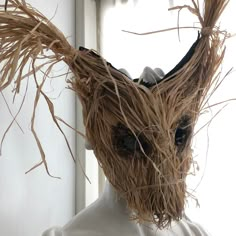 a head made out of straw with eyes and hair on it's face, sitting in front of a window