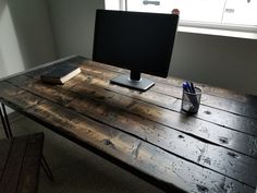 a computer monitor sitting on top of a wooden desk next to a cup and pen