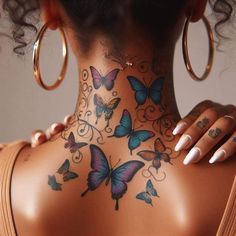 the back of a woman's neck with butterflies painted on her body and in gold hoop earrings