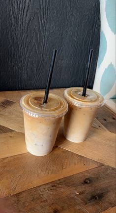 two iced coffees sitting on top of a wooden table next to a black wall