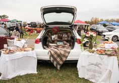 the back end of a car with food and drinks on it at an outdoor event