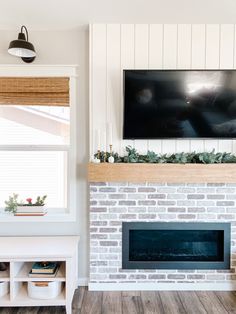 a flat screen tv mounted above a fireplace in a living room with white walls and wood flooring