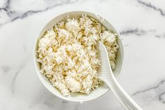 a white bowl filled with rice and a spoon on a marble counter top next to it