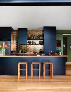 an open kitchen with wooden floors and dark blue cabinetry, along with bar stools