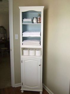 a tall white cabinet with towels on top