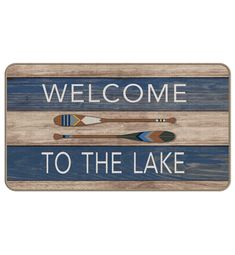 a wooden sign that says welcome to the lake with two paddles and an arrow