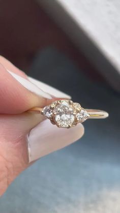 a woman's hand holding an engagement ring with three diamonds on it and the middle one is yellow gold