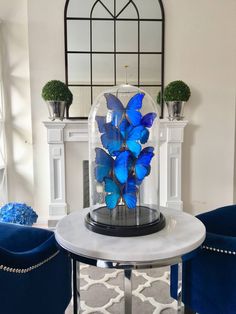 a glass vase filled with blue butterflies sitting on top of a table next to two chairs