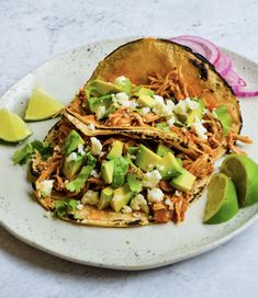 two tacos with shredded meat, avocado and cilantro on a plate