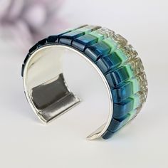 Handmade fused glass large cuff bracelet Bring a piece of ocean with you everywhere you go.Bright and deep ocean blue with clear aqua shimmer.Signature natural sandy bottom accent.7.5 inches (190mm) total exterior length.1.5inches (38mm) total width.Handmade silver plated base with 17 unique glass stones.Metal sealed with Everbrite coating for added protection.One-size fits most, 6.5 inch up to 7.5 inch wrist circumference.Incorporates Bullseye and CBS dichroic glass.Sculpted by hand and fused m Unique Blue Bangle Cuff Bracelet, Unique Blue Bangle, Large Cuff Bracelet, Deep Ocean, Glass Bracelet, Statement Bracelet, Dichroic Glass, Art Fashion, Ocean Blue