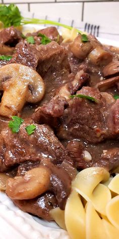 a white plate topped with pasta and meat covered in mushroom sauce next to parsley