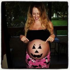 a pregnant woman is holding her belly up to show the shape of a halloween pumpkin