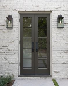 the front door to a white brick house with two lights on it's side