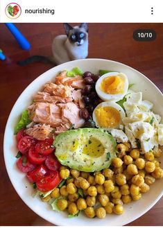 a white bowl filled with food on top of a wooden table next to a cat