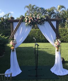 an outdoor wedding setup with white draping and flowers on the altar, microphone set up in foreground