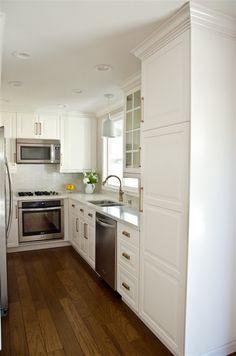 a white kitchen with stainless steel appliances and wood flooring is pictured in this image