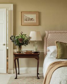 a bedroom with a bed, nightstand and flowers on the table in front of it