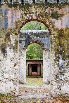 an old building with a brick archway in the center and trees growing out of it