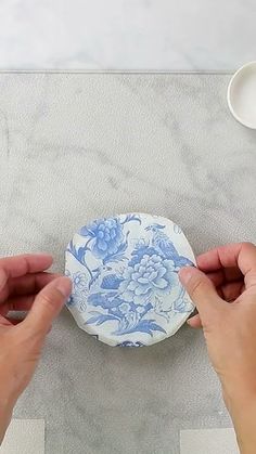 two hands holding a blue and white plate on top of a marble table with bowls