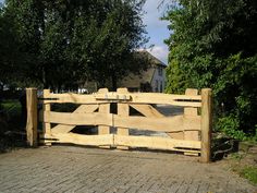 a wooden gate on the side of a brick road with trees in the back ground