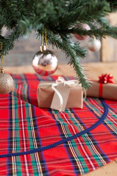 a christmas tree with presents under it on a plaid table cloth next to a wrapped present