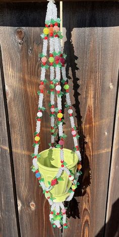 a yellow bucket hanging from the side of a wooden fence with beads attached to it