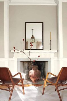 two chairs in front of a fire place with a vase on the fireplace mantel