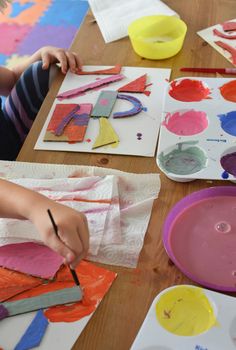 a child is painting on paper with paintbrushes and watercolors at a table