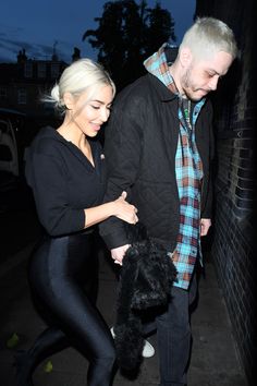 a man and woman walking down the street at night with one holding onto her coat