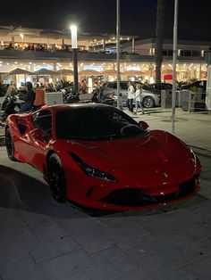 a red sports car parked in front of a building at night with people walking around