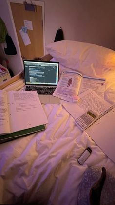 a laptop computer sitting on top of a bed next to an open book and notebook