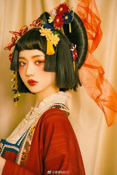 a woman with black hair wearing a red dress and flower headdress is standing in front of a curtain