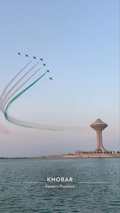 four jets are flying in formation over the water and a tower with a clock on it