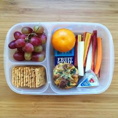 a plastic container filled with fruit, crackers and other food on top of a wooden table