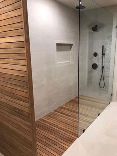 a walk in shower sitting next to a wooden floor and white tiled walls with glass doors