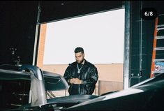 a man standing in front of a car looking at his cell phone while wearing a leather jacket