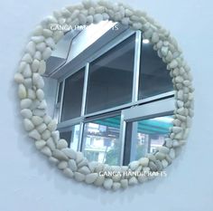 a circular mirror made out of rocks on the side of a wall next to a window