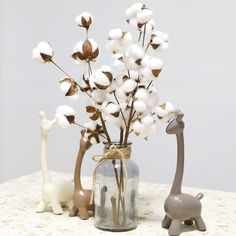 two small giraffes are next to a vase with cotton flowers in it