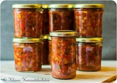 six jars of pickled tomatoes sit on a table