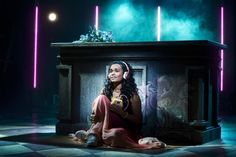 a woman sitting on the floor with headphones in front of a table and lights behind her