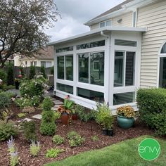 a white house with lots of plants and flowers in the front yard, on a cloudy day